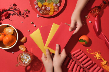 A hand is choosing a red envelope among many other lucky money envelopes. On the table, a plate of...