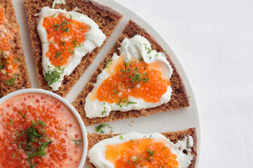 Appetizer with red caviar, sour cream, dill, onion and rye bread on the white table - the finnish recipe for a holiday food, flat lay in minimalistic style