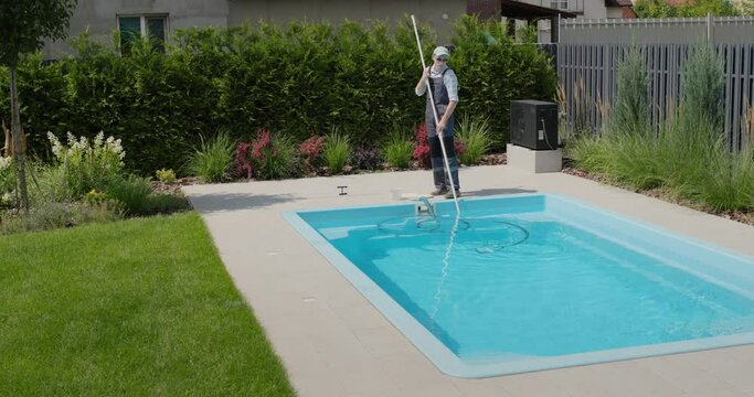 A worker cleans a swimming pool with a special vacuum cleaner.