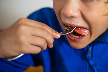 boy eats vegetable salad with a fork, mouth open wide
