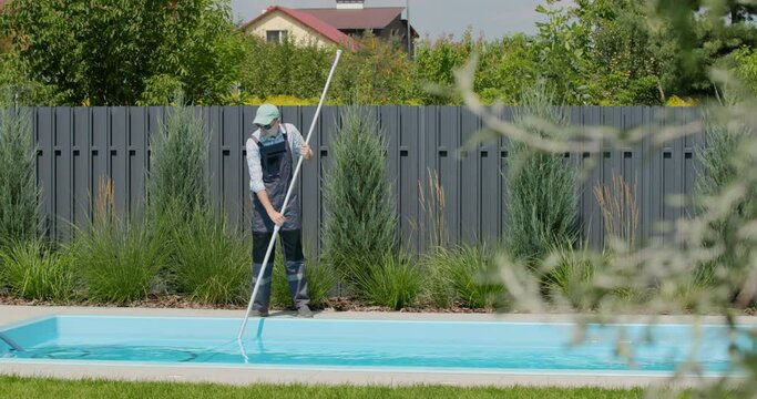 A worker cleans a swimming pool with a special vacuum cleaner.