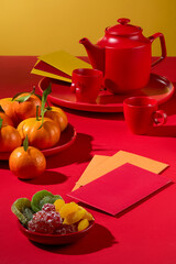 On a red background, a close-up captures a Tet tea set, tangerines, dried fruits, and lucky money envelopes arranged on plates-a festive Tet tea table adorned with delightful snacks.