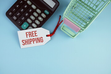 Top view of Free Shipping text on tag sale with calculator and shopping trolly cart flat lay on...