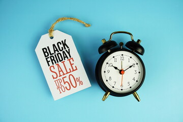 Top view of Black Friday sale 50% text on tag sale with black alarm clock flat lay on blue background