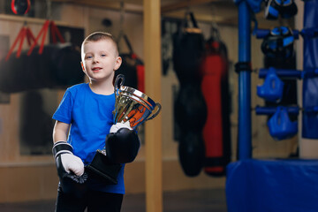 Winner boxer boy in black boxing gloves with gold cup on background ring sport gym for kid