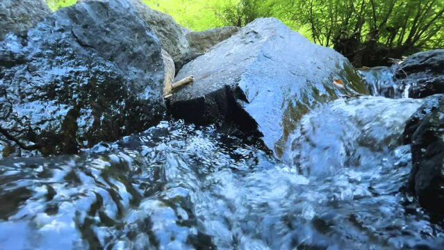 A stream flows quickly in a green forest in summer. A small waterfall emerged from beneath the rock. with crystal clear water Take photos in slow motion