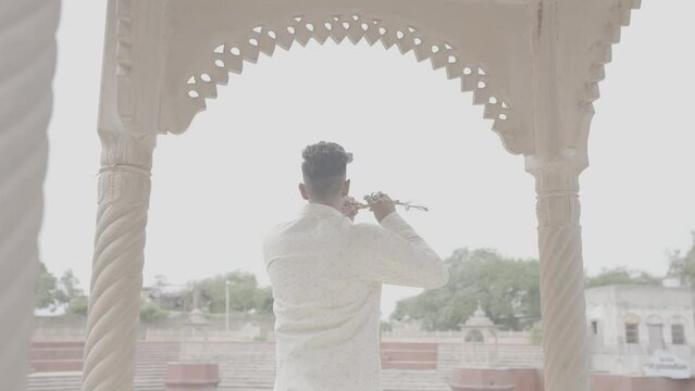 An Indian man's soulful flute resonates along the tranquil banks of the pond, weaving a melody that echoes the essence of nature and tradition.4k footage