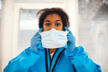 Portrait of young tired african american medical worker or nurse in protective gear taking off face...