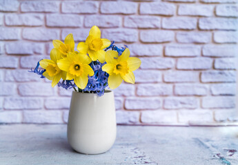 Yellow narcissus flowers bouquet in vase on white bricks background 