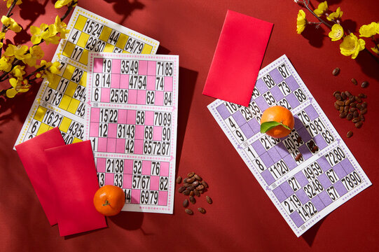 View from above of a set of lotto, red envelopes, tangerines, melon seeds and yellow apricot flower branches displayed on a red background. Copy space. - Powered by Adobe