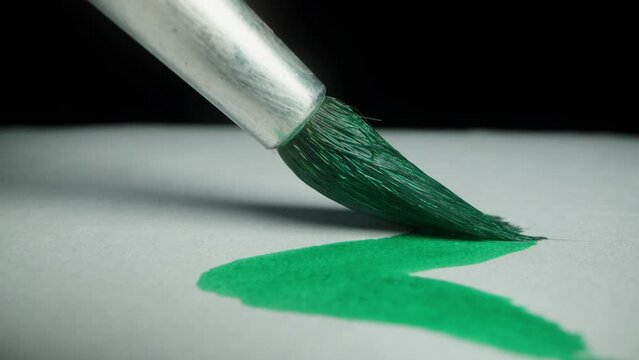 Brush with green paint glides on the canvas. On a black background. Macro from a first-person perspective.
