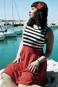 Harbor pin-up: Red skirt, stripes, retro glasses. Red heels, secrets beneath: garter belt, nude sheer stockings. Reimagined vintage elegance. 