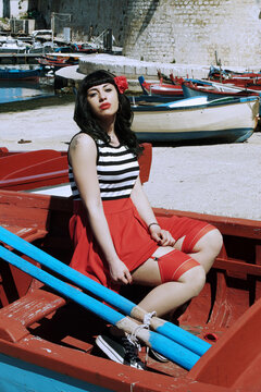Harbor pin-up: Red skirt, stripes, retro glasses. Red heels, secrets beneath: garter belt, nude sheer stockings. Reimagined vintage elegance. 