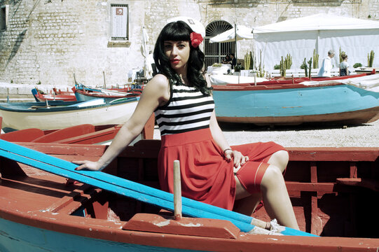 Harbor pin-up: Red skirt, stripes, retro glasses. Red heels, secrets beneath: garter belt, nude sheer stockings. Reimagined vintage elegance. 