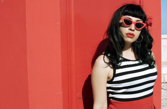 Port harbor pin-up: Red skirt, stripes, retro glasses. Red heels, intriguing secrets beneath: garter belt and sheer stockings. Revisited vintage elegance.