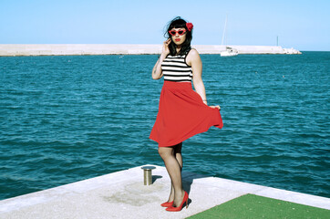 Port harbor pin-up: Red skirt, stripes, retro glasses. Red heels, intriguing secrets beneath:...