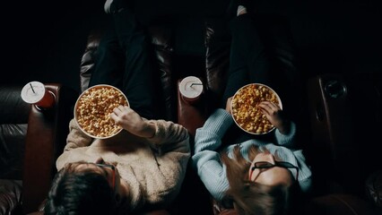 Couple in love A guy and a girl eat popcorn and watch a movie in a cinema using 3D glasses. Concept of a movie show in a cinema