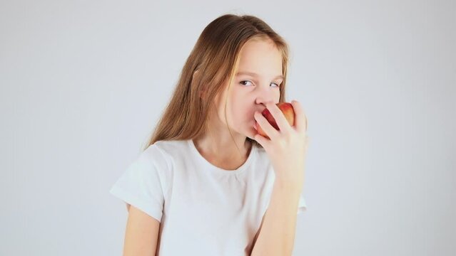 Pretty girl with long hair eating red apple over white background. Time for snack.