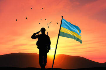 Silhouette of a soldier with the Rwanda flag stands against the background of a sunset or sunrise....