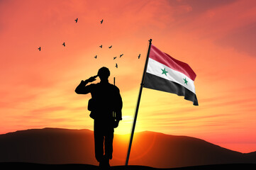 Silhouette of a soldier with the Syria flag stands against the background of a sunset or sunrise....