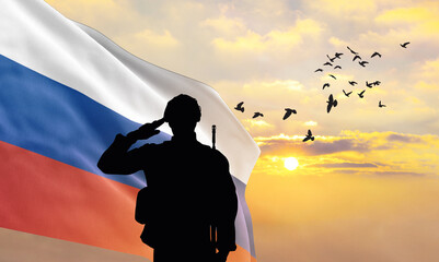 Silhouette of a soldier with the Russia flag stands against the background of a sunset or sunrise....