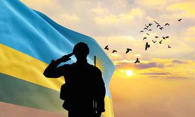 Silhouette of a soldier with the Rwanda flag stands against the background of a sunset or sunrise....