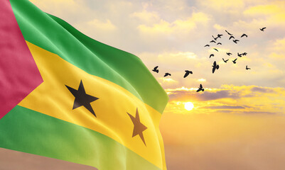 Waving flag of São Tomé and Príncipe against the background of a sunset or sunrise. São Tomé...