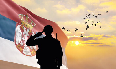 Silhouette of a soldier with the Serbia flag stands against the background of a sunset or sunrise....