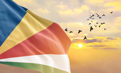 Waving flag of Seychelles against the background of a sunset or sunrise. Seychelles flag for Independence Day. The symbol of the state on wavy fabric.