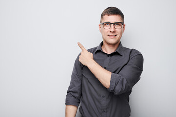 Handsome man in glasses pointing aside finger, demonstrating empty space for product or text...