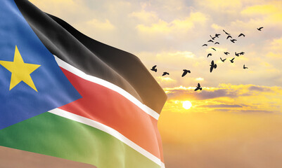 Waving flag of South Sudan against the background of a sunset or sunrise. South Sudan flag for...