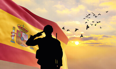 Silhouette of a soldier with the Spain flag stands against the background of a sunset or sunrise....