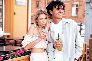 Young smiling beautiful woman and her handsome boyfriend in casual summer clothes. Happy cheerful family. Female having fun. Couple posing in street. Holding and drinking cocktail drink in plastic cup