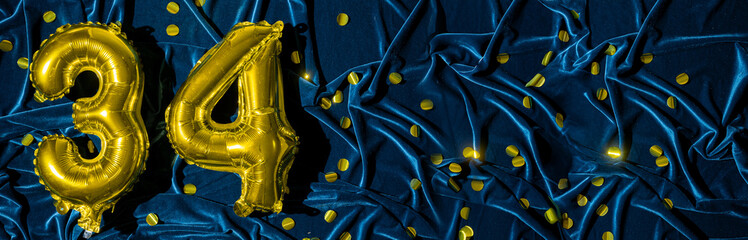number thirty four, gold foil balloon number on blue velvet background with confetti. Birthday...