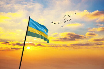Waving flag of Rwanda against the background of a sunset or sunrise. Rwanda flag for Independence Day. The symbol of the state on wavy fabric.