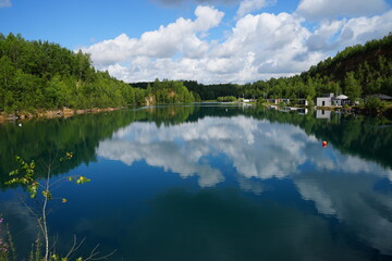 jezioro o przezroczystej wodzie pośród lasu oraz odbijające niebo