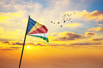 Waving flag of Seychelles against the background of a sunset or sunrise. Seychelles flag for Independence Day. The symbol of the state on wavy fabric.