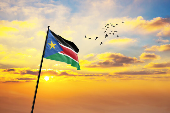 Waving flag of South Sudan against the background of a sunset or sunrise. South Sudan flag for Independence Day. The symbol of the state on wavy fabric.