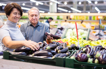 Couple standing in salesroom of greengrocer and choosing eggplant