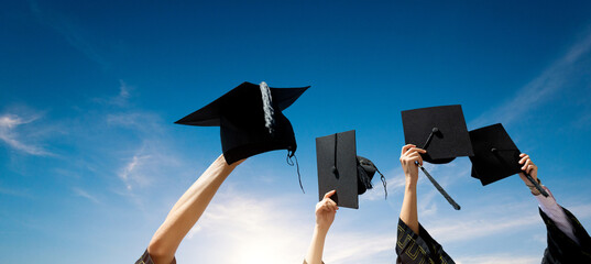 Four hands holding graduation hats against blue sky