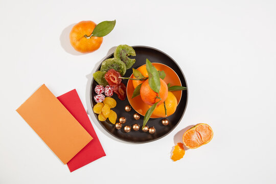 Top view of jam and tangerines on a black tray, two lucky money envelopes on a white background. Simulate the Tet tea table. Images for advertising.