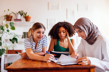 Three cute teenage girls do their homework. Caucasian, African American and a Muslim female teens...