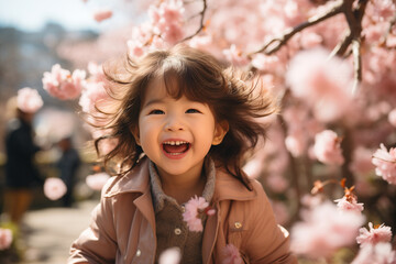 Bella bambina di origini asiatiche corre felice in mezzo ai fiori di ciliegio in primavera - obrazy, fototapety, plakaty