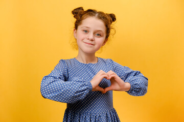 Portrait of pretty happy preteen caucasian girl showing heart gesture and smiling to camera,...