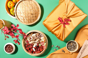 Bamboo steamer holds tangerines, jam, jujubes and gummy candy. Melon seeds and sunflower seeds are stored in small bowls, a gift box and a vase of flowers are displayed.