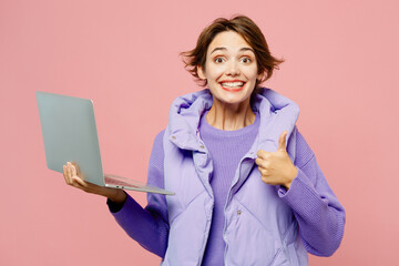 Young amazed happy IT woman wearing purple vest sweatshirt casual clothes hold use working on laptop pc computer show thumb up isolated on plain pastel light pink background studio. Lifestyle concept.