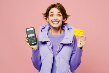 Young woman she wear purple vest sweatshirt casual clothes hold wireless modern bank payment terminal to process acquire credit card isolated on plain pastel light pink background. Lifestyle concept.