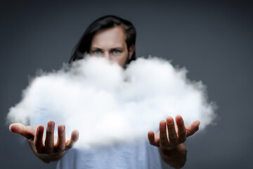 guy with a cloud. a young guy with dark long hair and a white T-shirt stands on a dark background and holds a large cloud in his hands, creative concept