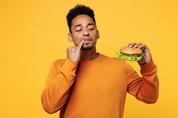 Young minded thoughtful man he wear orange sweatshirt casual clothes eat burger touch lips with...