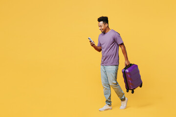 Traveler man wears casual clothes hold bag suitcase use mobile cell phone isolated on plain yellow...